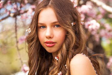 Naklejka premium Young girl posing near blossom cherry tree with pink flowers