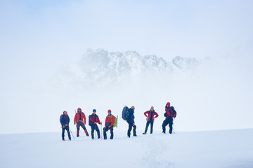 Hikers team standing on hillside valley covered with snow. Male alpinists and trekking sticks enjoying the view of winter mountains while taking rest break during hike, looking to the camera