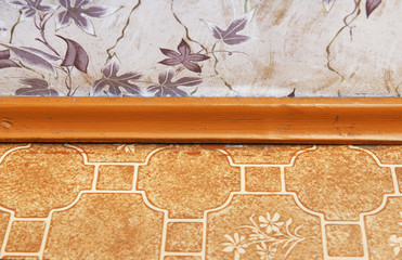 Old wallpaper on the wall and old linoleum on the floor, between them a red floor plinth of red color.