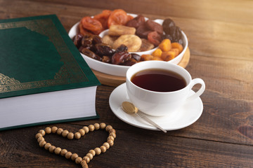 Koran, plate of dried fruit, Cup of tea, heart, prayer beads on wooden table, Ramadan, iftar concept