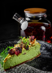Close up view of a piece of pistachio cheesecake in plate on black wooden table background