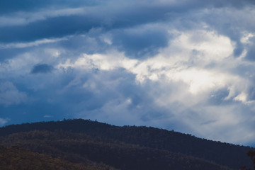 Fototapeta premium Australian mountain landscape with clouds and intense sunrays, shot in Tasmania over Mount Wellington