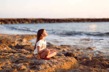 Fototapeta na wymiar child meditates sitting on stones at sea sunset