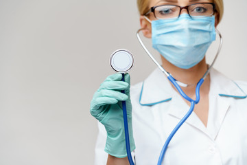 female doctor with stethoscope wearing protective mask and latex gloves over light grey background