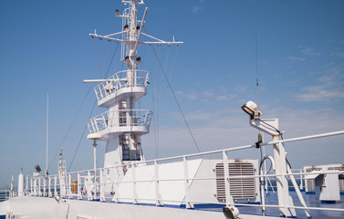 A large metal mast of a white ship. Barrier and ship's deck. Sunny, summer day.