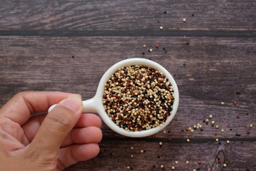 Close up hand holding the white cup with quinoa seeds on wooden table background. Quinoa is a good source of protein for people following a plant-based diet. 
