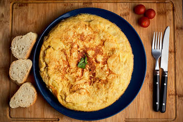 potato omelette on wooden board with bread and tomatoes