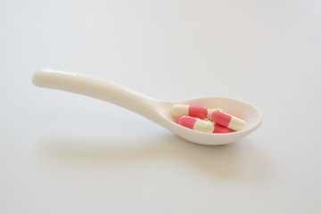 White and pink capsule or Pill in the white spoon isolated on white background. Medicine and healthy concept.