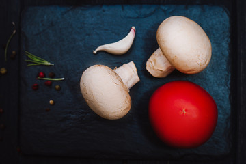 Mashrooms, tomato, garlic and spice on black stolen plate on black wooden background