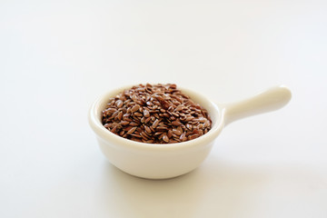Brown Flax seeds or Linseeds or Common flax in the white bowl isolated on white background. Flax seeds are rich of omega fat.