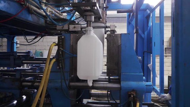 The process of blowing plastic tanks in extrusion equipment. Molten white plastic like a tube is placed in a press form and blowing the air and is give to shape of the bottle