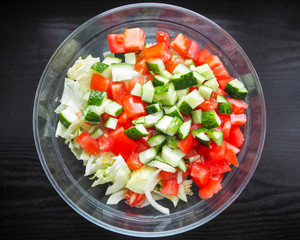 round transparent glass bowl with sliced iceberg lettuce cucumber tomato and onion on a dark background . vegetarian salad gluten-free cooking