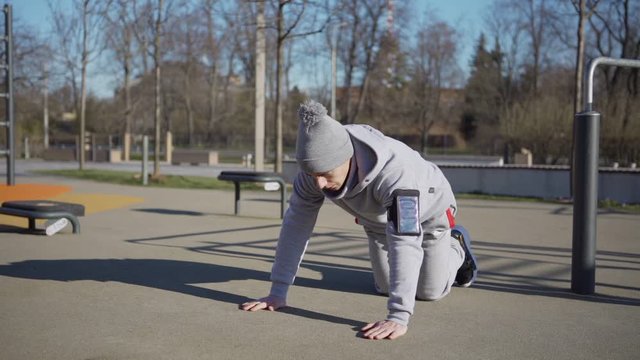 Strong young man doing clapping pushup exercise in slow motion at street workout spot outdoors, armband with cellphone on his arm