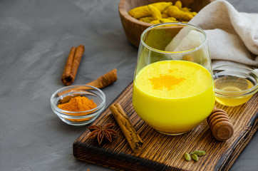 Golden milk in a glass on a wooden board with honey and other spices. A healthy drink made from milk and turmeric. Horizontal orientation. Copy space.