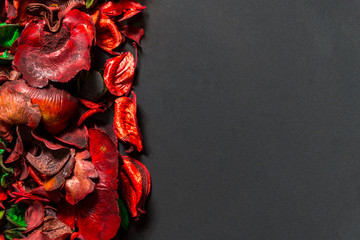 Red potpourri flowers and leaves on ceramic plate on black background, top view