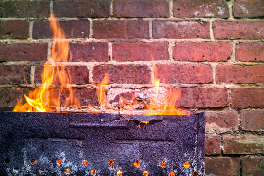 Fire And Grill Over Red Brick Wall Background In Backyard