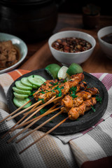 focused on chicken satay on stone plate with striped napkin and slice of cucumber with dark surrounding