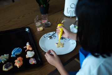 Defocused back portrait of girl decorating the cookie surface by squeezing the liquid sugar