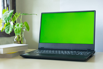 Fototapeta premium Laptop computer showing chroma green screen on LCD display stands on a desk with books next to ready for further design and copy space.
