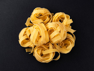 Raw fettuccine pasta isolated on black background, top view