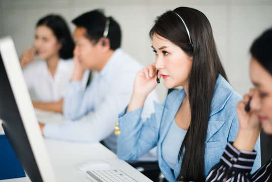 Young beautiful Asian operator woman with headsets working with team in call center.Customer support phone looking computer with feeling serious .Team operator call center service concept.