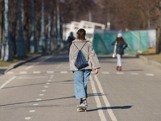 People in the Sparrow Hills/ Vorobyovy Gory park  in the spring time. Few people. They are hurry up. Young woman skateboarding. Coronavirus Pandemic lifestyle. Back / rear view.