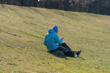 Naklejka na ściany i meble Couple of young woman and man sitting on the grass in Vorobyovy Gory / Sparrow Hills park in spring time. Coronavirus Pandemic lifestyle of the big city