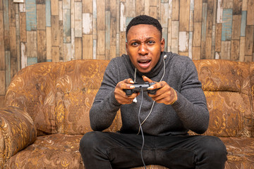young black man immersed in playing video games sitting on a couch at home