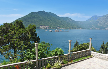 Daytime summer view from the ancient stone terrace on the Boka Kotor Bay of the Adriatic blue sea against the dark mountains of Montenegro.