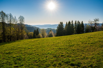 Fototapeta na wymiar green field in the mountains with a valley below and the sun on the horizon, czech