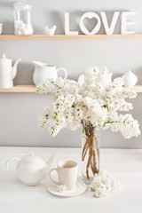 Bouquet of white lilac in vase and tea set on table in kitchen. Happy birthday greeting card. Hello spring and summer. Greeting card for Women's Day and Mother's Day. Spring season, copy space