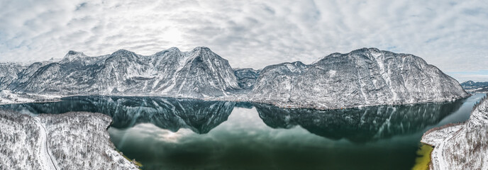 Aerial panoramic drone shot of Hallstatt village by lake surrounded by snow mountains with couds during winter