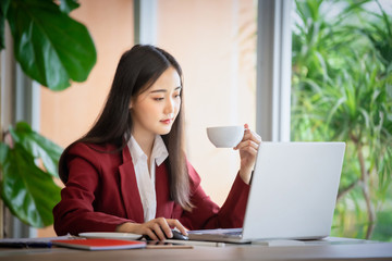 Portrait of Young asian businesswoman sitting indoors in cafe drinking coffee using laptop computer. Business success concept.