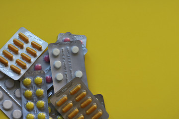 Capsules and pills packed in blisters on yellow background.