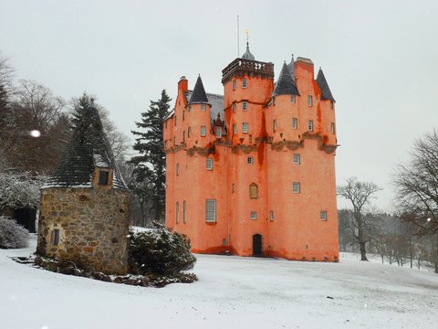 Hermoso paisaje cubierto de nieve en las Tierras Altas de Escocia de un castillo color naranja y una casa de campo de piedra rodeados de &aacute;rboles