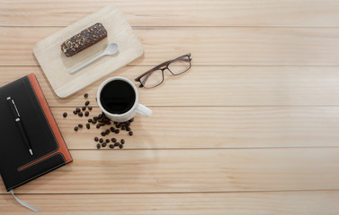 Wooden office desk with a cup of coffee, served with chocolate and glasses on the side, top view, Morning life at work concept.