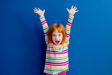little girl with red hair in a multicolored smile stands on a blue background