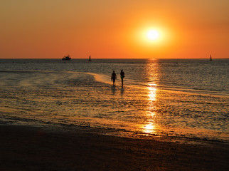 Fototapeta na wymiar Beautiful and colorful sunset with silhouettes of two people walking by the sea. Sundown in a beach in Sanlucar de Barrameda, Cádiz, Andalucia, Spain.