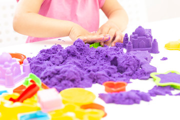 Obraz na płótnie Canvas Childrens hands plays kinetic sand in quarantine. purple sand on a white table. coronavirus pandemic