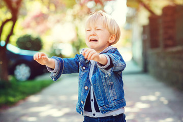 Sweet blond child boy crying outdoors. Little son pulls the handles to mom.