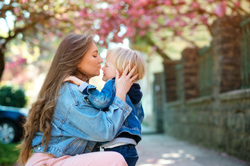 Mother soothing her sad child outdoors. Mom with upset baby on a walk at spring street.