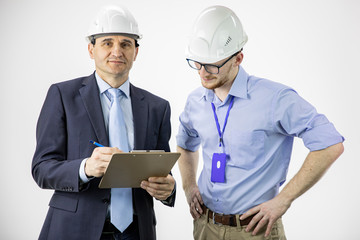 Head of project holds clipboard looks with smile in camera, discusses product details with chief engineer isolated on white background. Engineers meeting for architectural project, team work