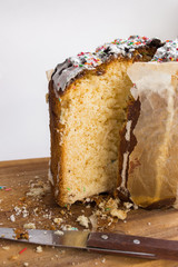 Orthodox festive Easter cake in parchment baking paper cut with a knife on a cutting wooden board decorated with white icing and sweets of different colors
