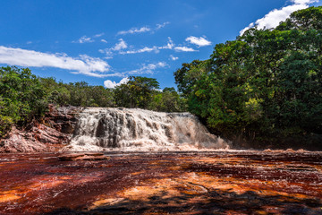 Red water at the stunning Presidente Figueiredo waterfall (Reserva Ecológica Cachoeira Santuário) surrounded by green rainforest on a clear blue sunny day near Manaus, Amazon in Brazil, South America