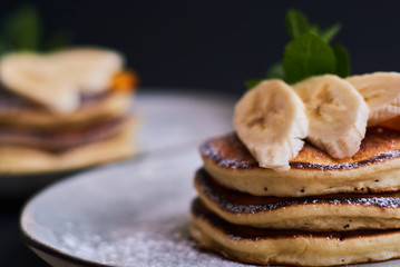 Homemade breakfast of pancakes decorated with orange, banana, mint and sugar powder on black background in grey plate.