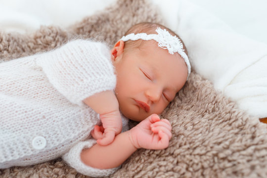 Newborn baby in white knitted suit sleep in wooden basket. Child resting in cute pose. Tiny girl with tender headband on head. Creative infant photography