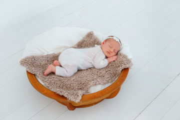 Newborn baby in white knitted suit sleep in wooden basket. Child resting in cute pose. Tiny girl...
