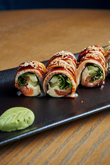 Traditional japanese sushi roll with eel, cucumber, cream cheese and salmon on a black plate. Close up. Food photo for menu