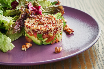 Appetizing, fresh salad with quinoa, avocado and tomatoes in a purple plate on a wooden background. Healthy Salad for Diet Food
