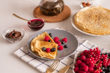 Two homemade folded pancakes with honey and berries on served kitchen table